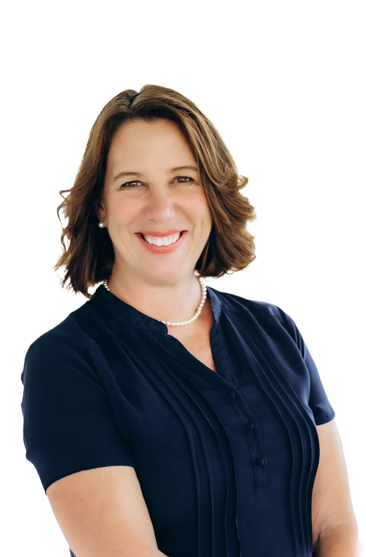 Smiling woman with brown hair in a navy blouse and pearl necklace, standing against a white background.