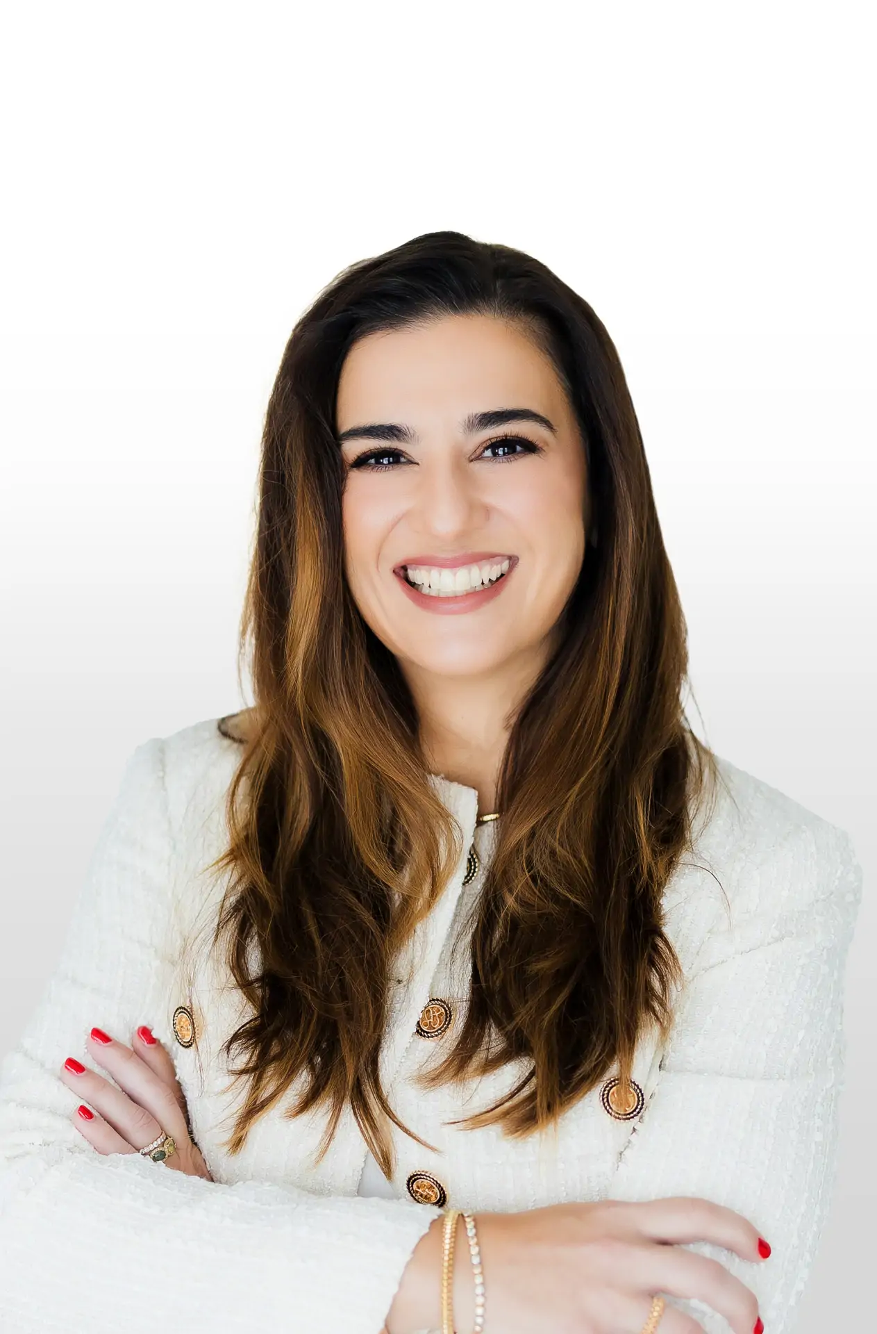 Woman with long brown hair in a white jacket, smiling with arms crossed against a plain white background.