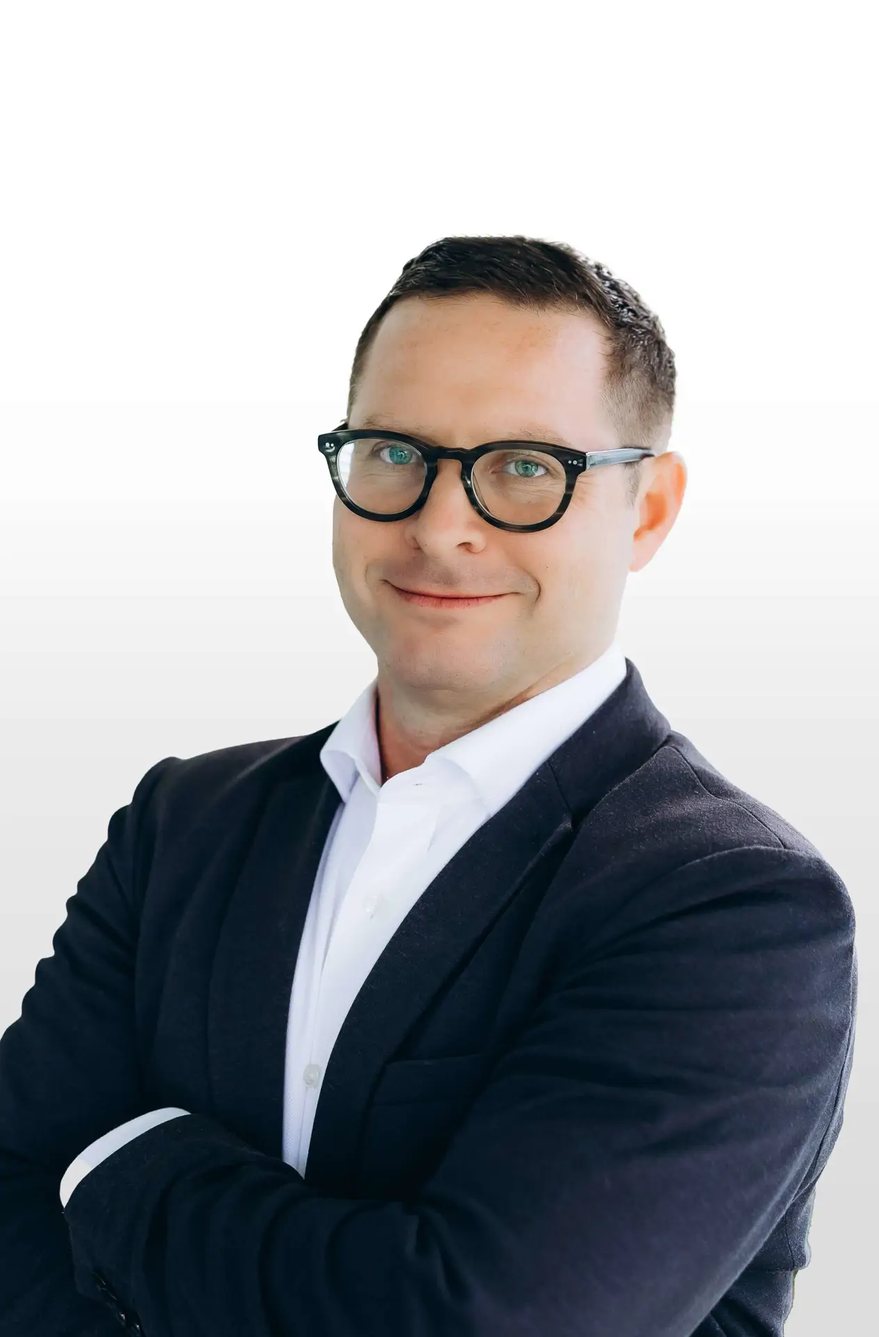 Man wearing glasses and a dark suit jacket, smiling with arms crossed against a plain white background.