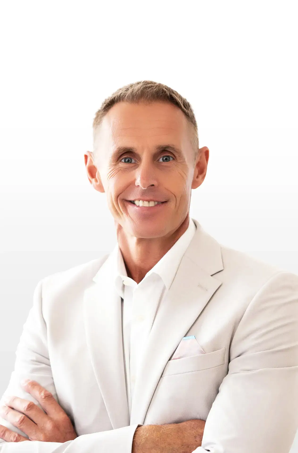 Smiling man in a light suit with arms crossed, standing against a white background.